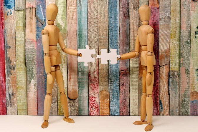 Image of two wooden figures interacting, representing teamwork